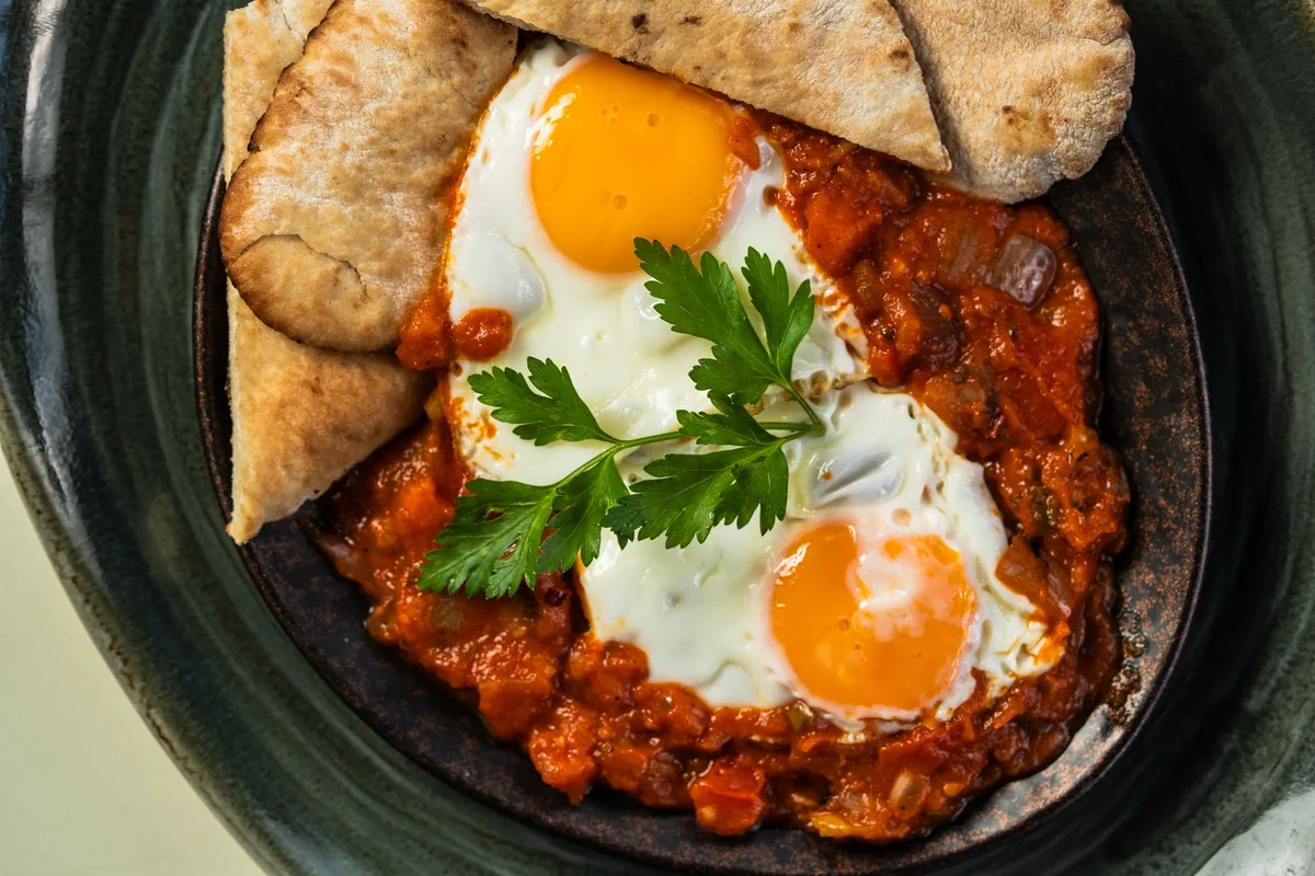 Œufs cuits dans une sauce tomate aux poivrons, pain pita