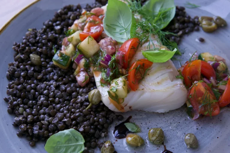 Filet de poisson blanc sur des lentilles noires, tomates et herbes